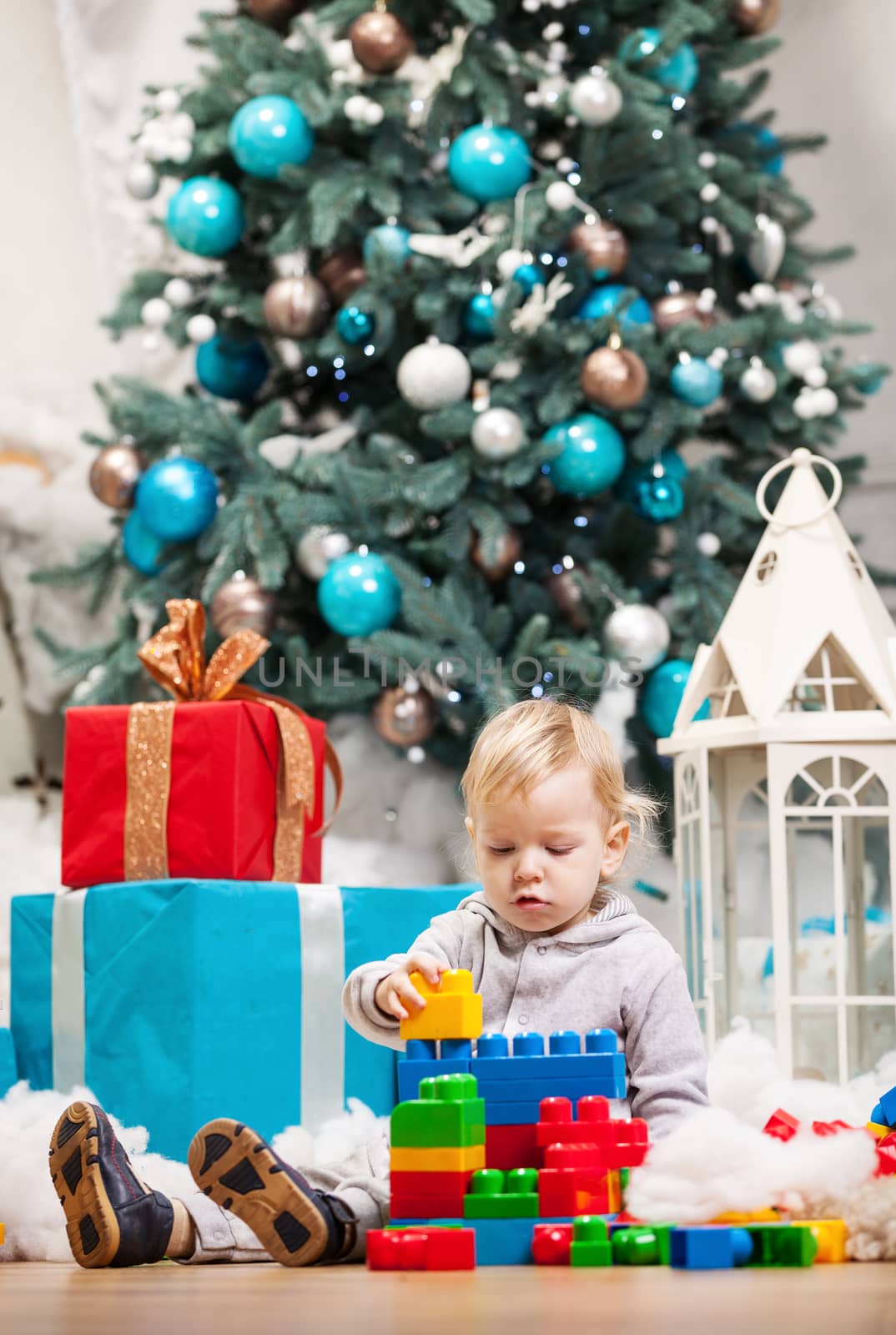 Cute toddler boy playing with building blocks at Christmas tree