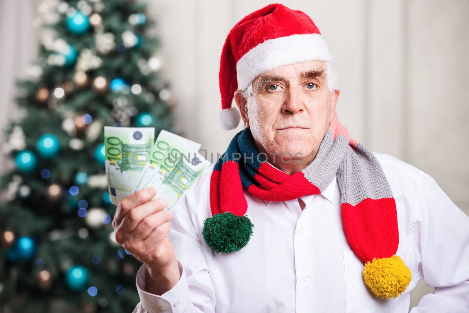 Senior man in Santa's hat holding money by photobac