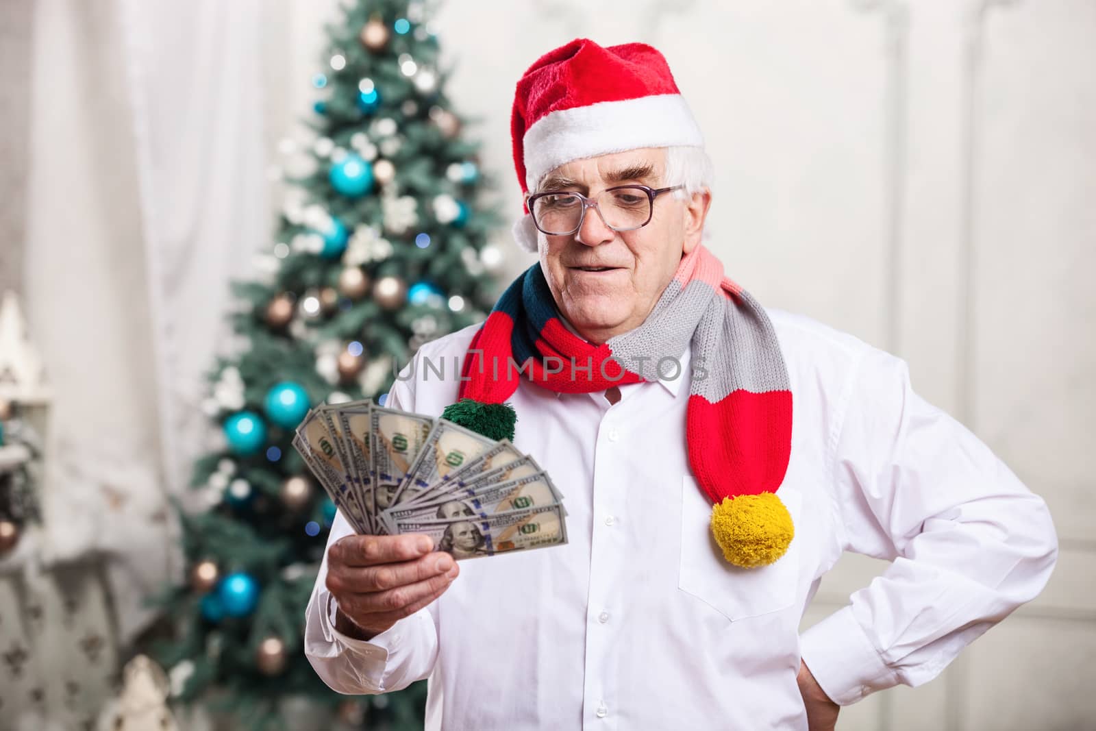 Senior man in Santa's hat holding money against Christmas background