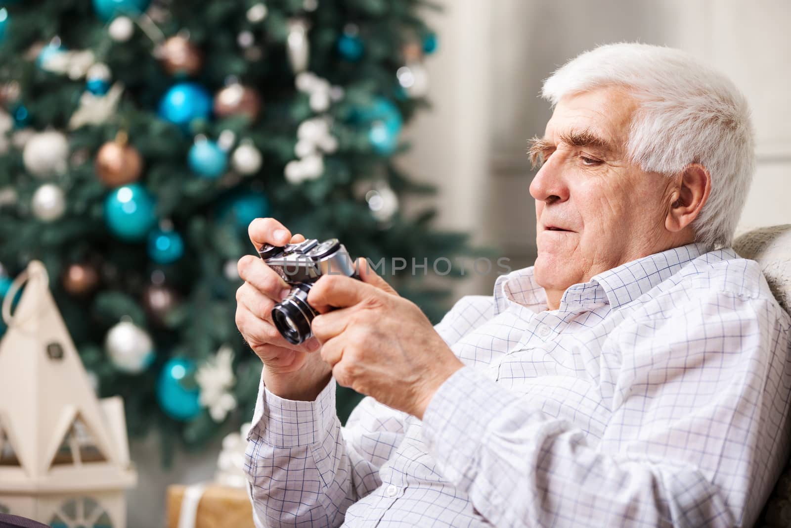 Senior man looking at display of retro style camera and smiling against Christmas background