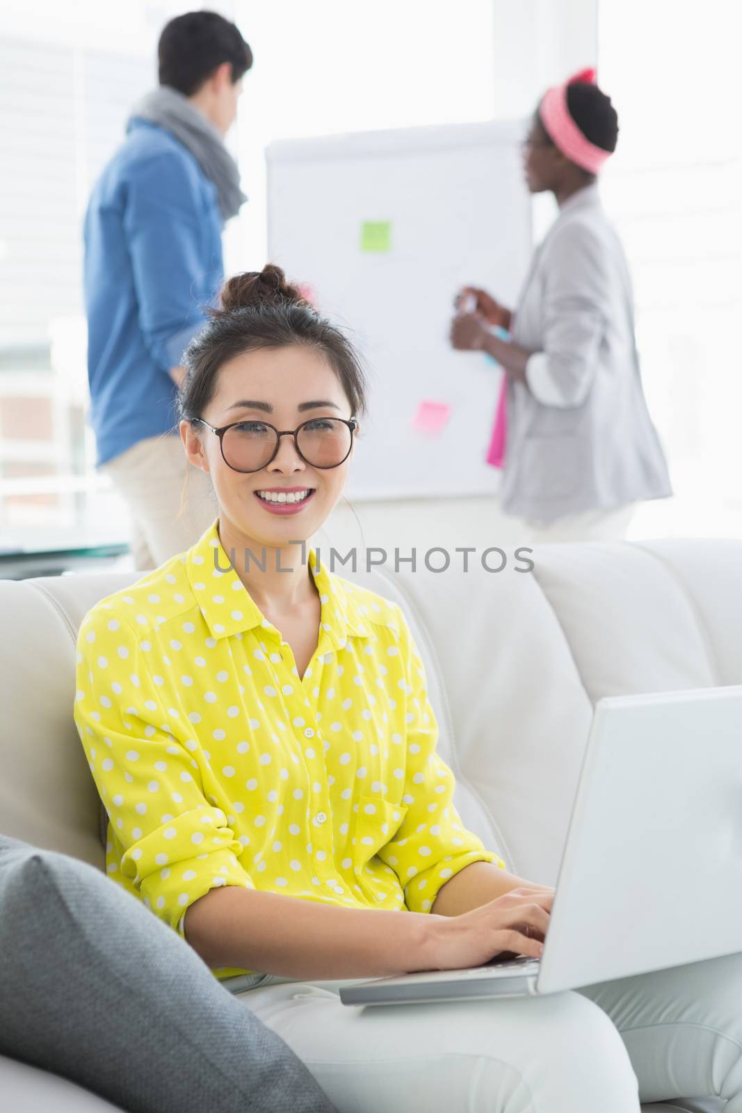 Young creative woman using laptop on couch in creative office