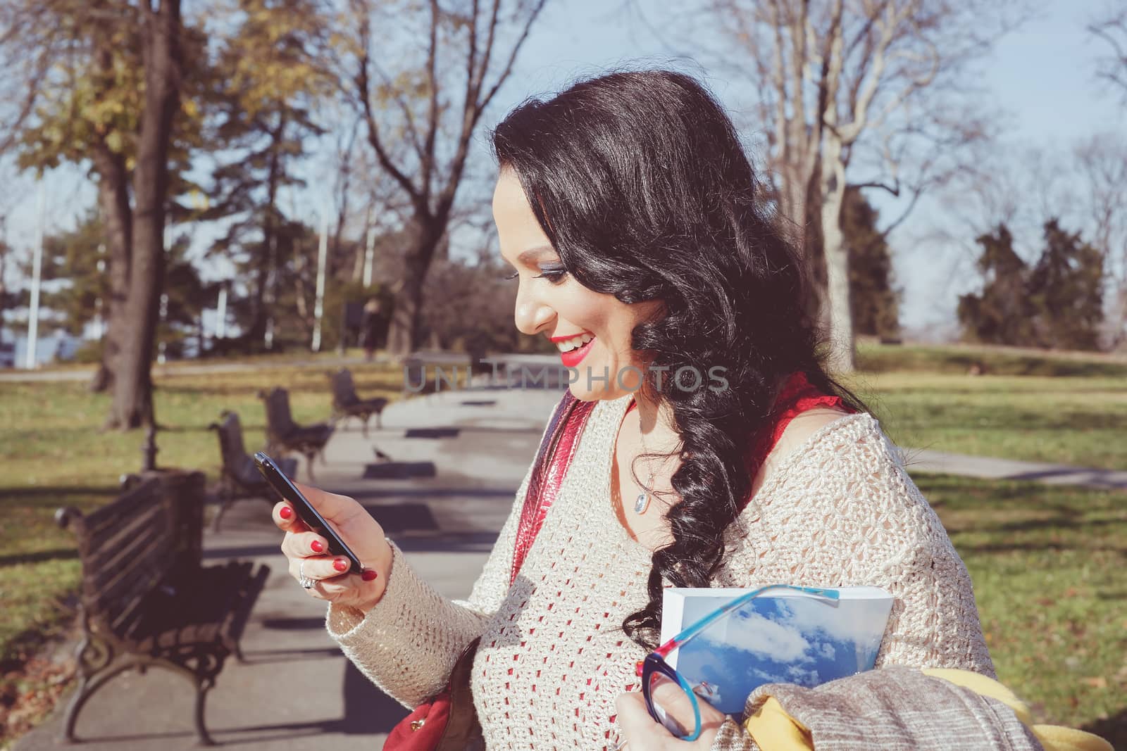 Woman text messaging on a mobile phone in a park on sunny day.