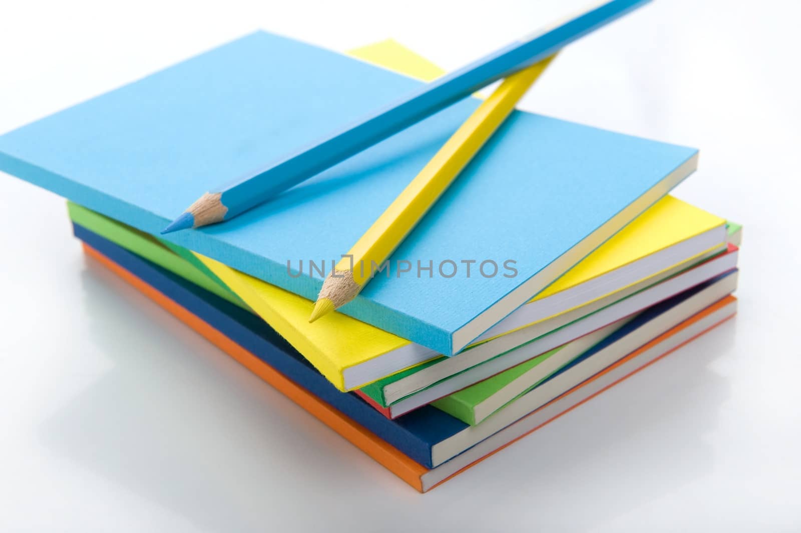 Horizontal isolated on white background close-up of blue and yellow pencils on top id workbook pile