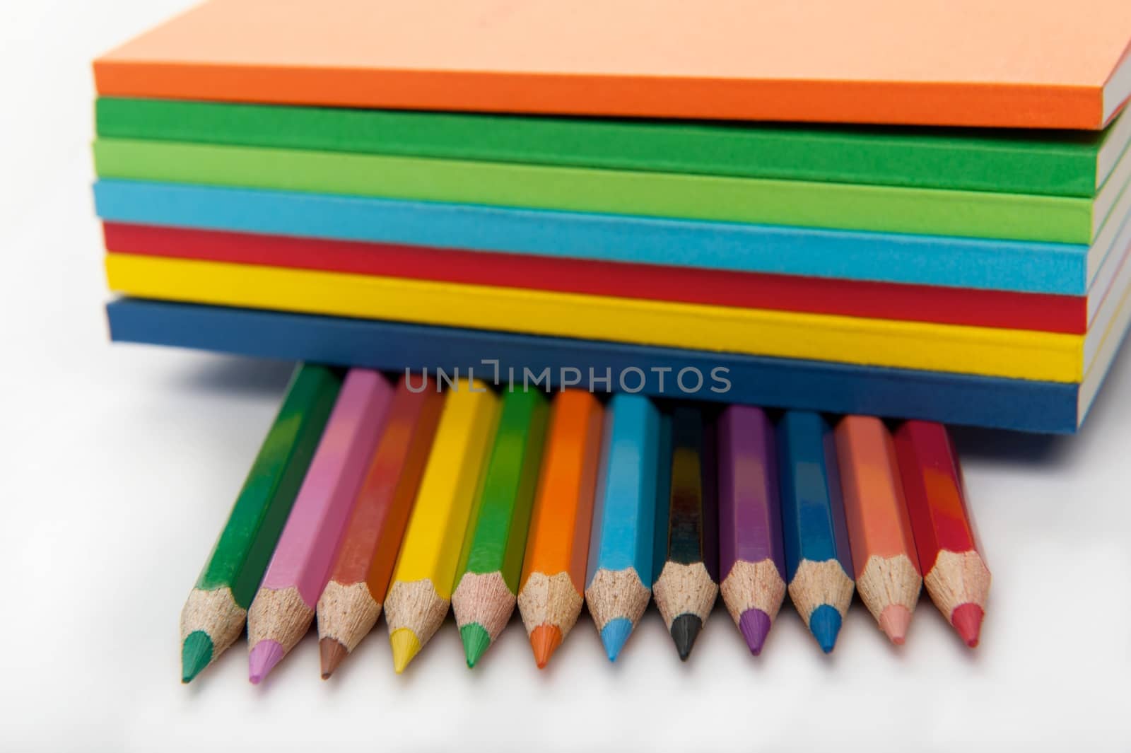 Isolated on the white background horizontal shot of seven notepads put on top of twelve colored pencils
