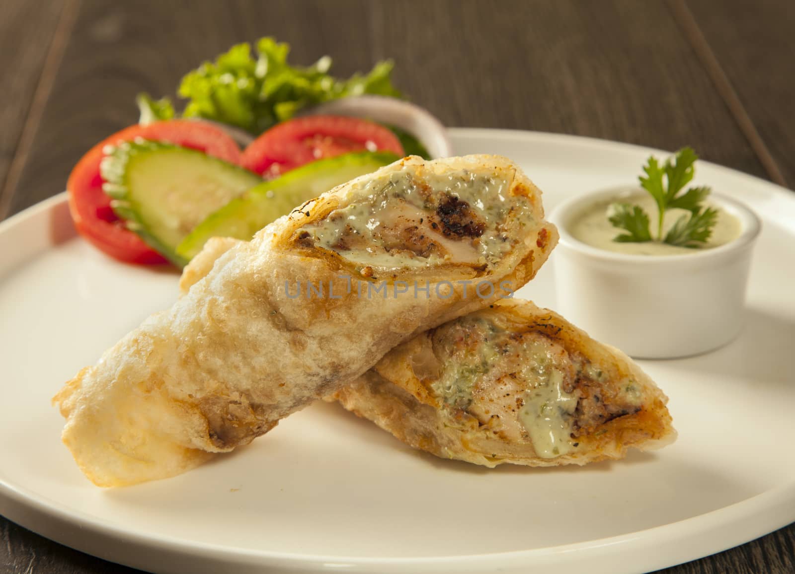 Traditional roll kebab paratha tikka wrap served on a plate with chutney and salad, on a wooden background