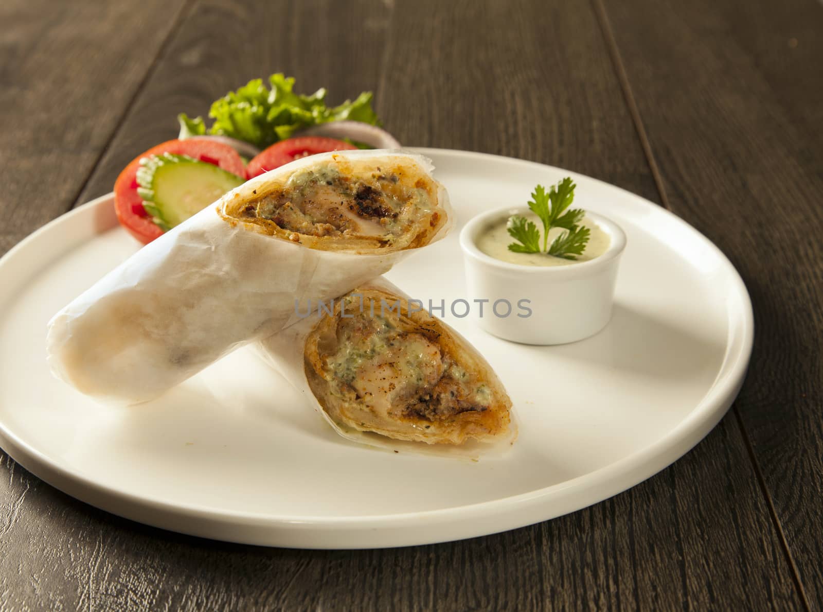 Traditional roll kebab paratha tikka wrap served on a plate with chutney and salad, on a wooden background