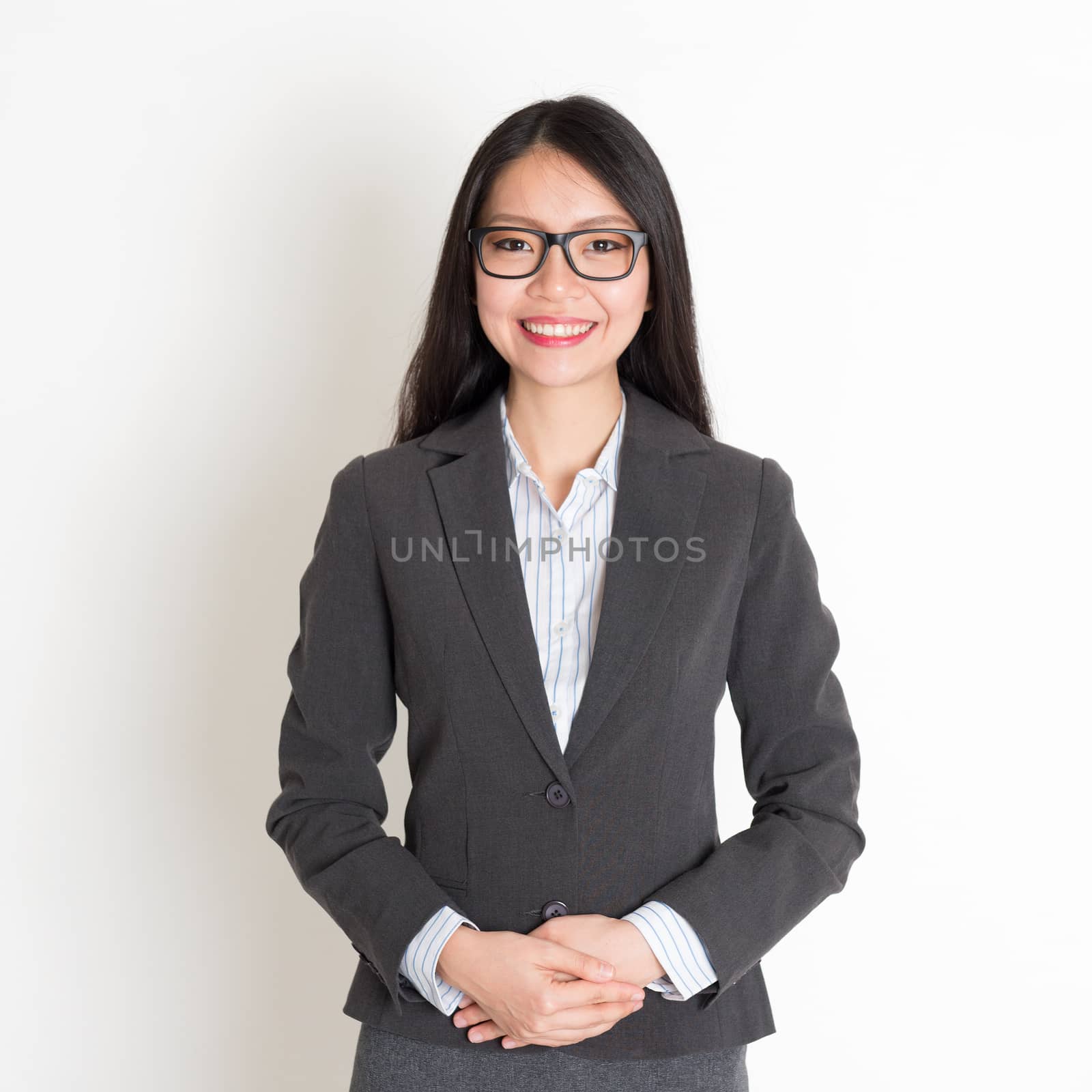 Asian business woman smiling at camera, standing on plain background.