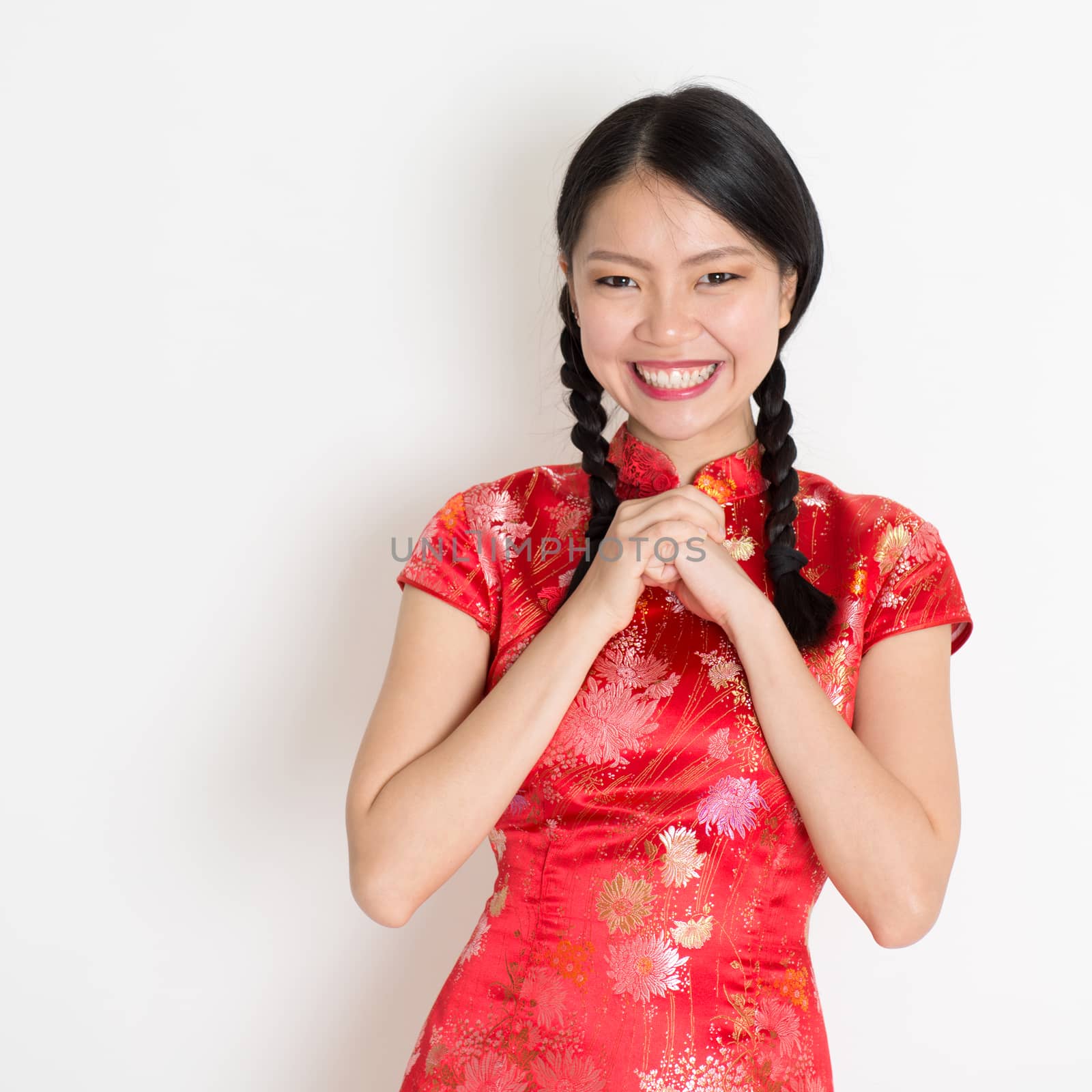Happy Chinese New Year!! Portrait of Asian Chinese girl greeting, in traditional red qipao standing on plain background.
