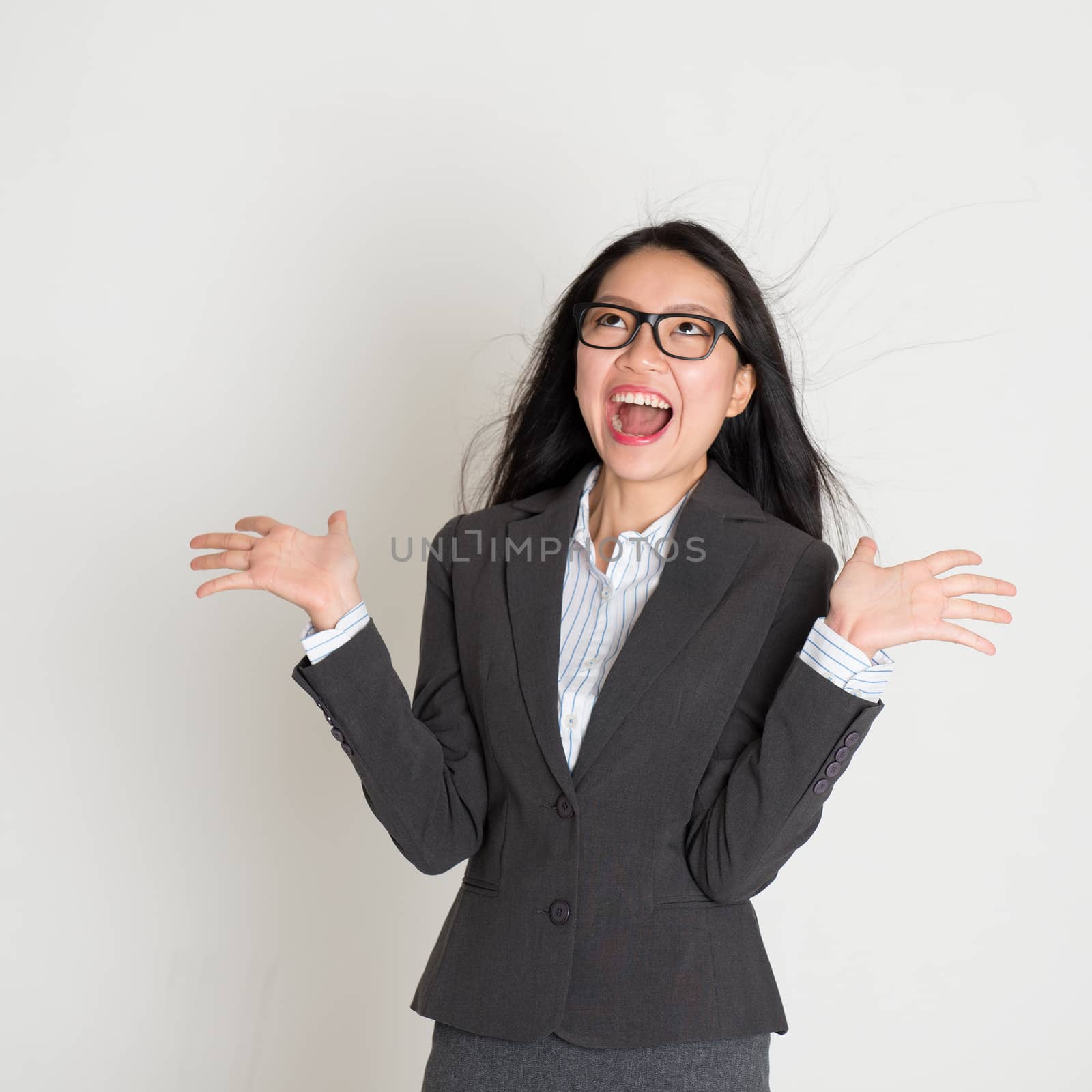 Young Asian business woman looking up and smiling, open palms standing on plain background.