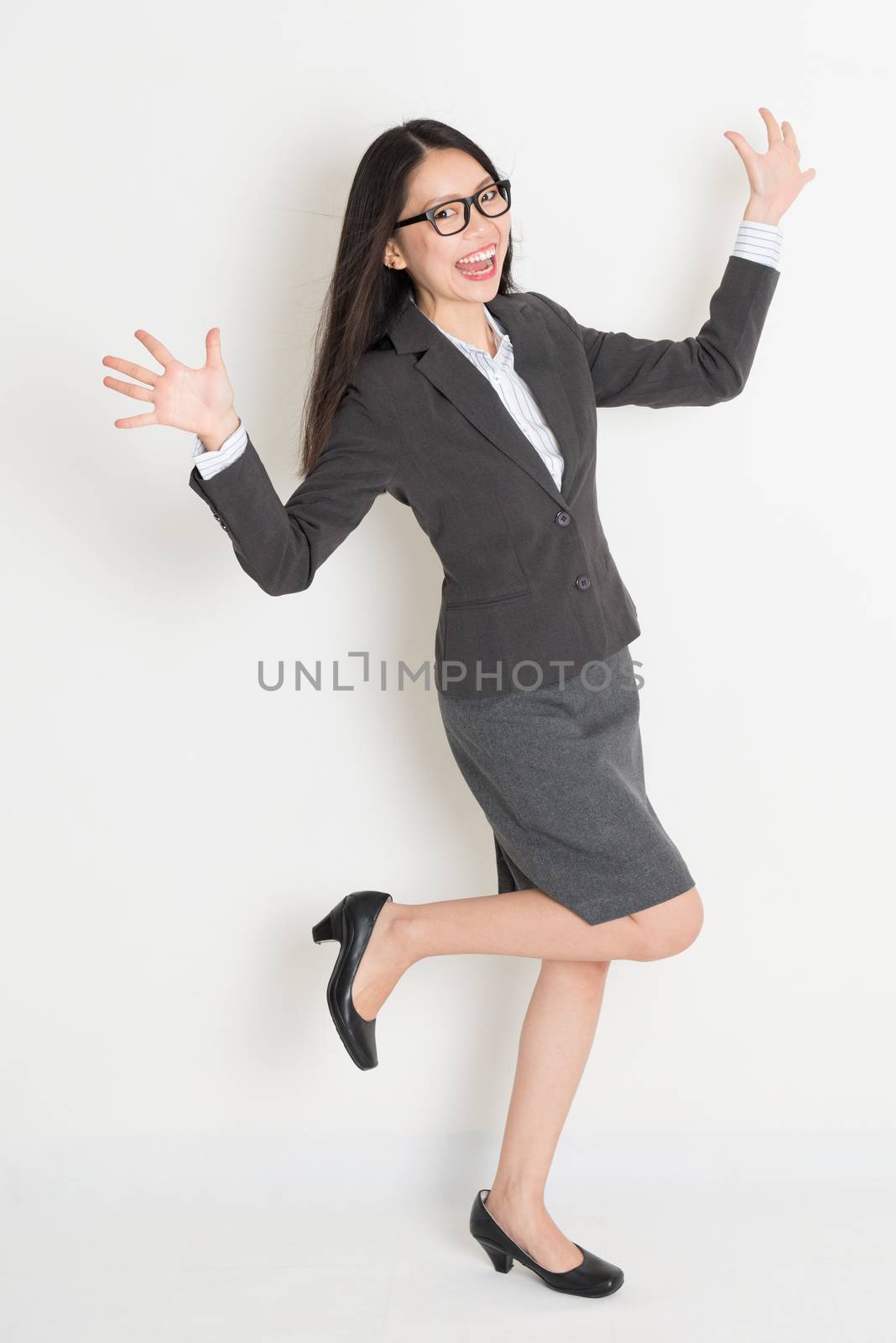 Excited full body Asian business woman standing on plain background.