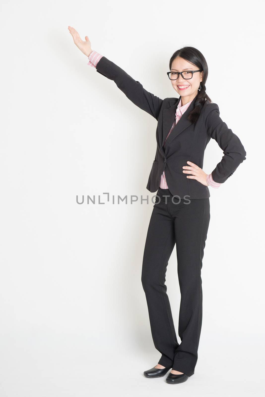 Full body Asian business woman showing copy space, standing on plain background.