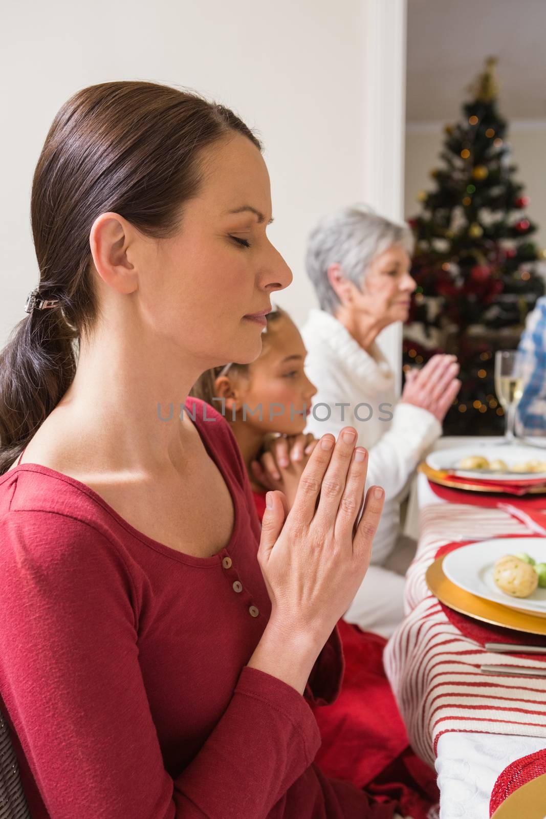 Extended family praying before christmas dinner at home in the living room