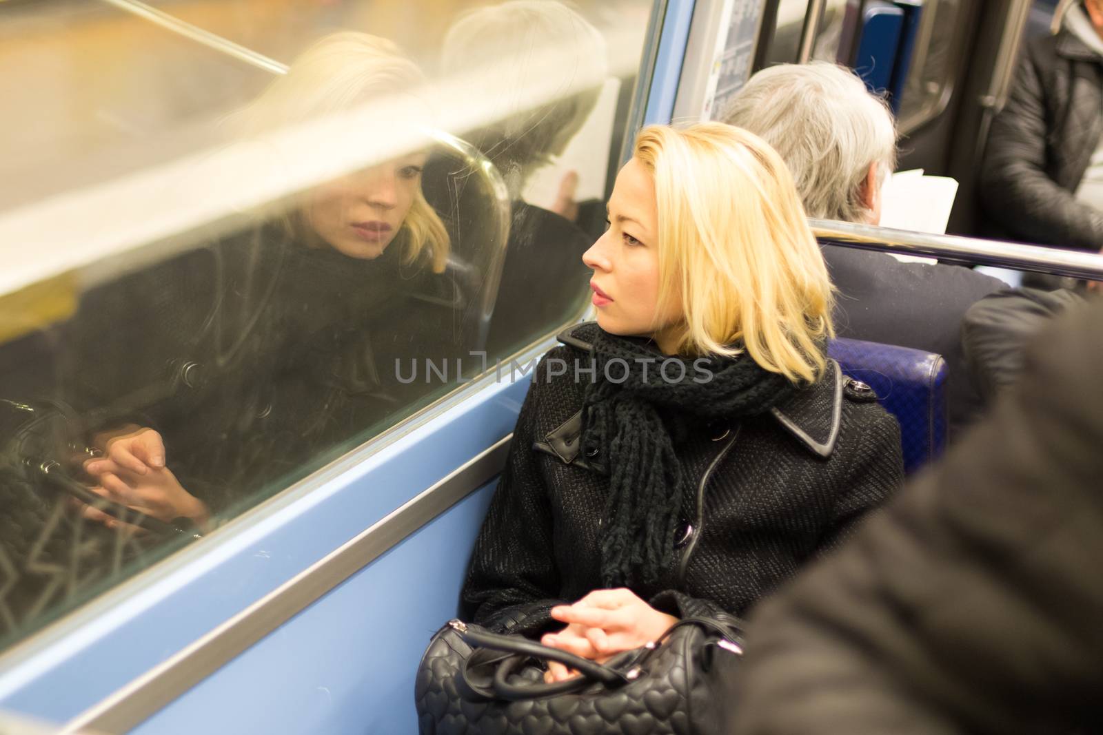 Thoughtful lady riding on a subway and looking out the window. Reflection of her face can be seen in the window.