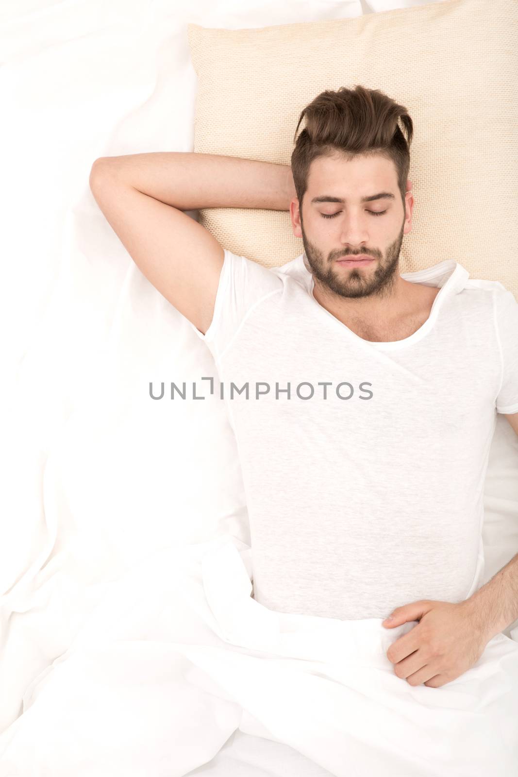 Portrait of a young man from above sleeping in a white bed.

