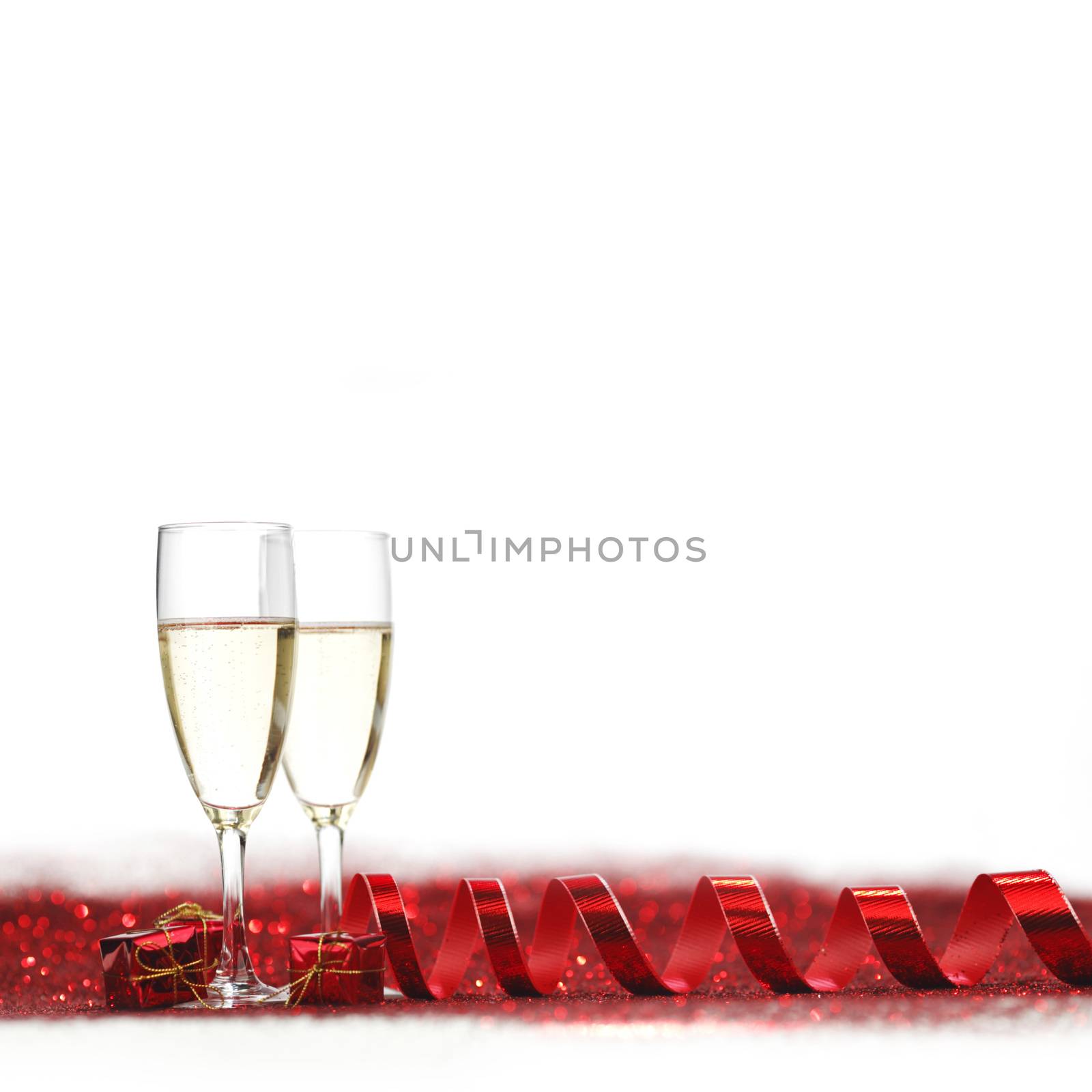 Glasses with Champagne and gifts on red glitters isolated on white background