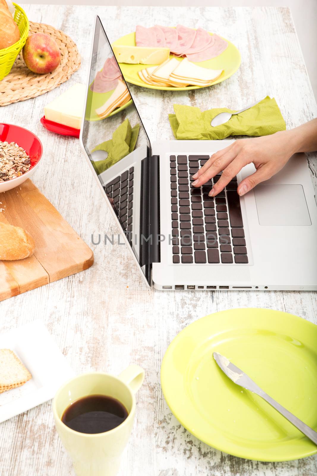 A young woman having breakfast while using a laptop computer.
