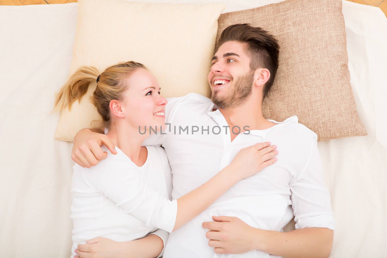 A happy young couple hugging in bed.
