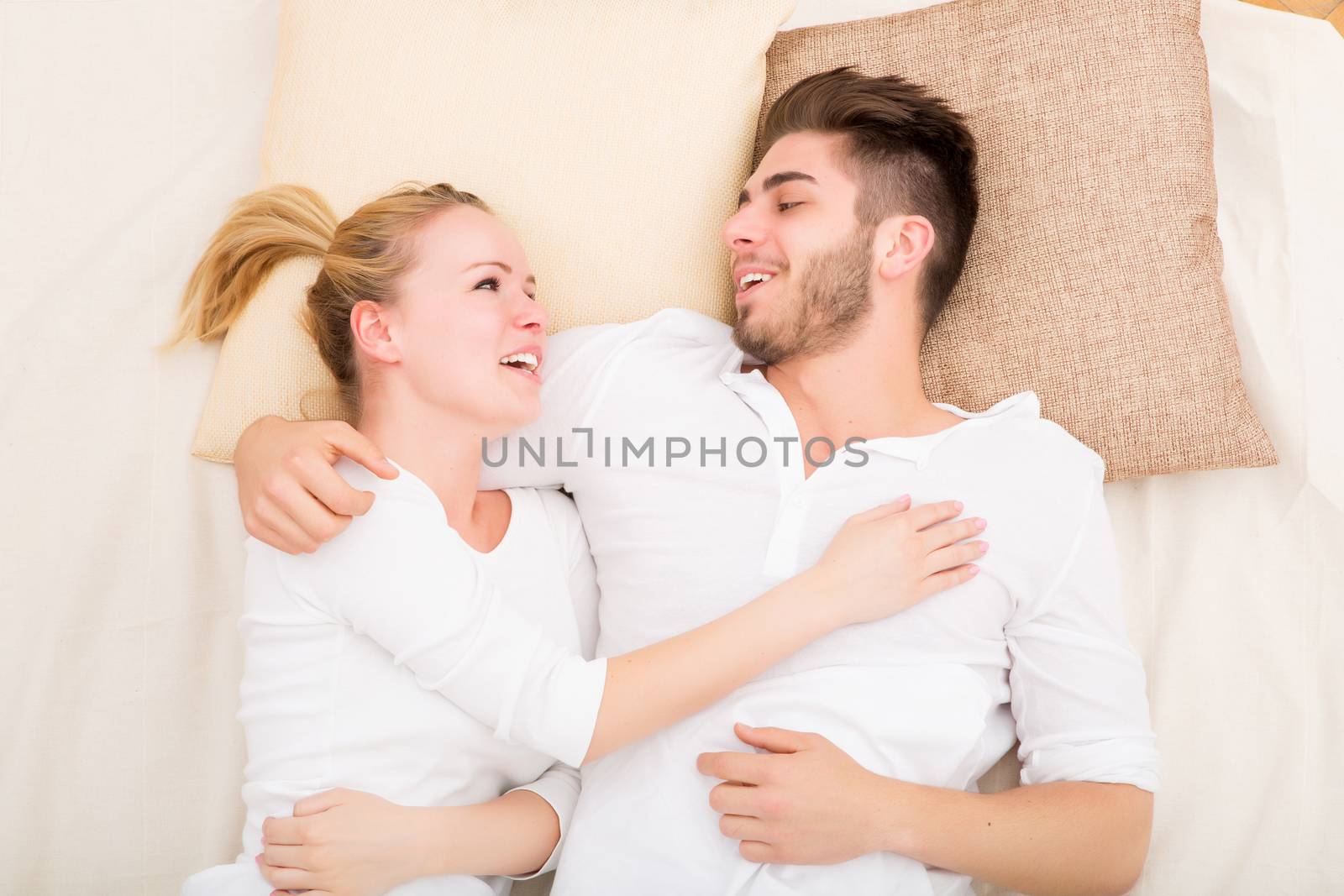 A happy young couple hugging in bed.
