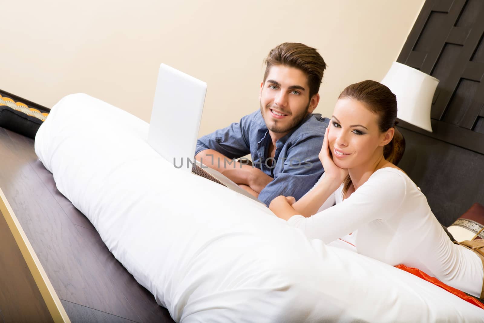 Young couple using a notebook in a asian hotel room while lying on the bed.
