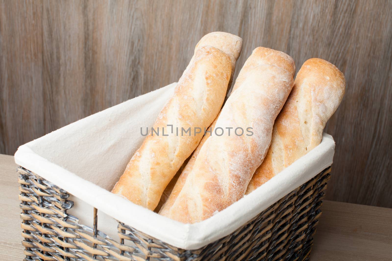 Stack of traditional fresh-baked French bread loafs baguette served in woven basket on wooden background