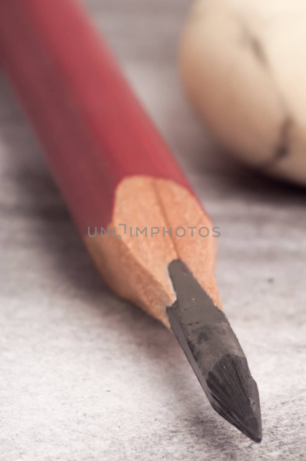 Pencil, sharpened in the way an artist would do, lying on a piece of paper already worked on with the pencil, and in the background an eraser.