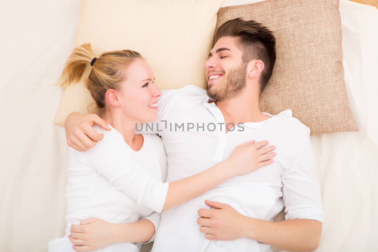 A happy young couple hugging in bed.
