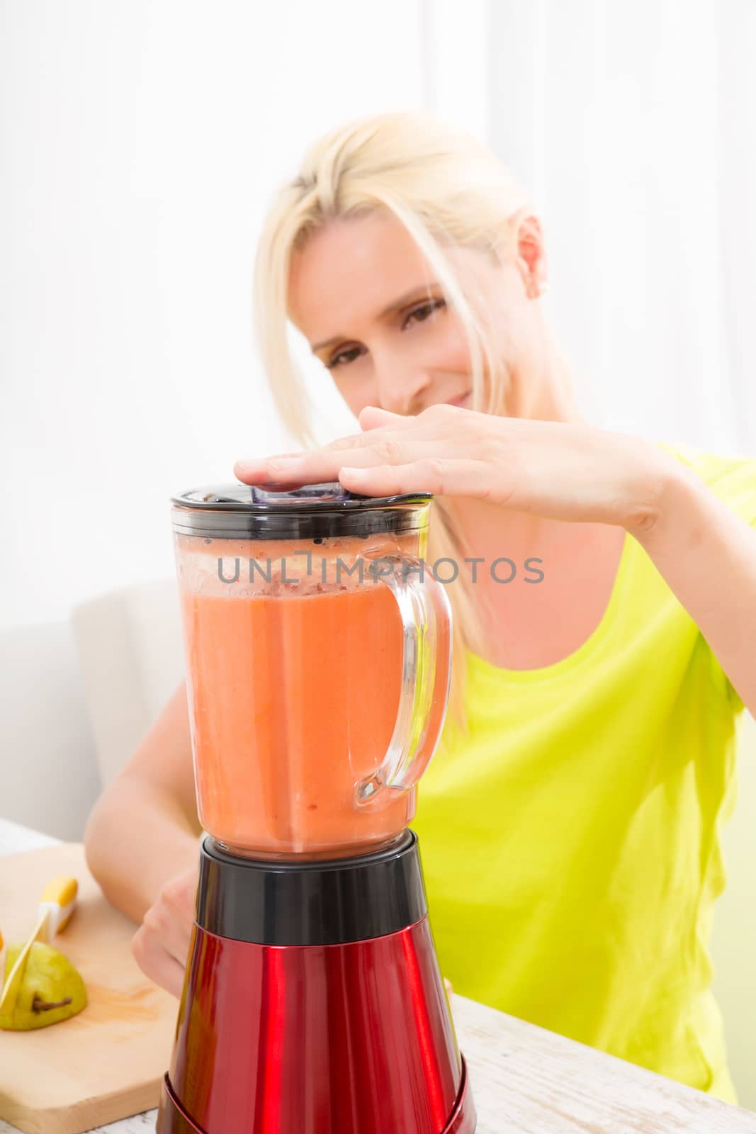 A beautiful mature woman preparing a smoothie or juice with fruits in the kitchen.
