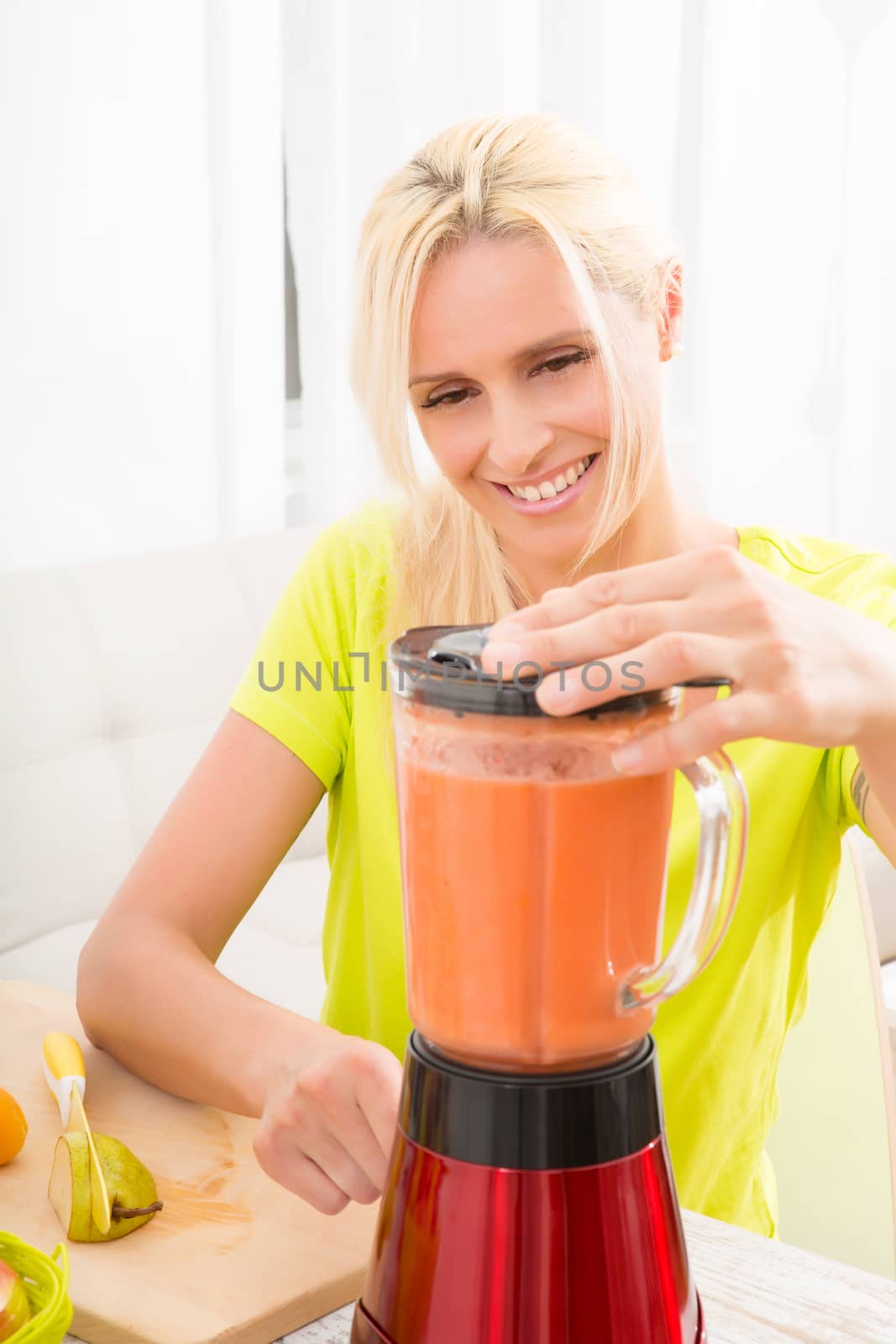 A beautiful mature woman preparing a smoothie or juice with fruits in the kitchen.
