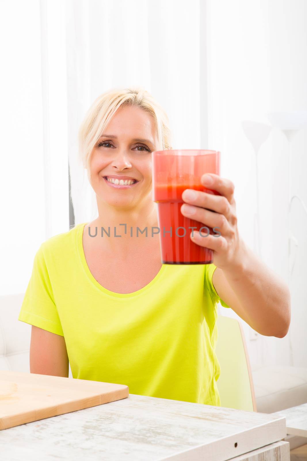 A beautiful mature woman enjoying a smoothie or juice with fruits in the kitchen.
