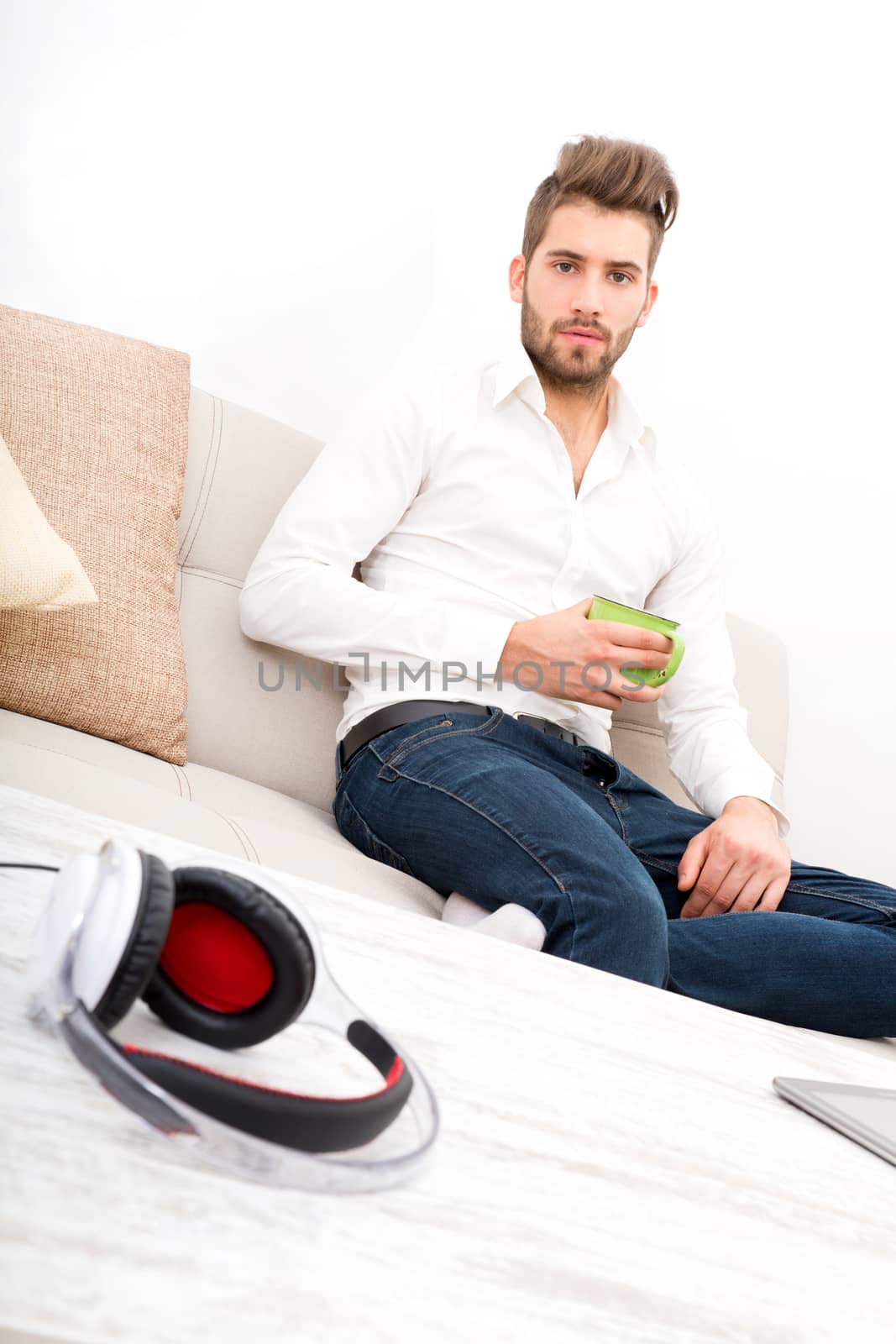A young adult man sitting on the couch holding coffee.
