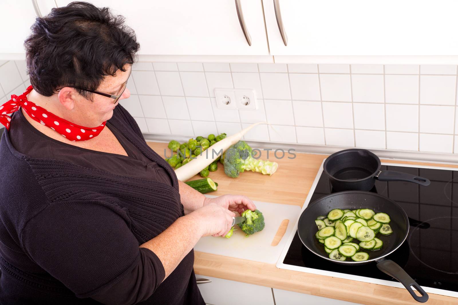 Mature overweight woman cutting vegetables in the kitchen.
