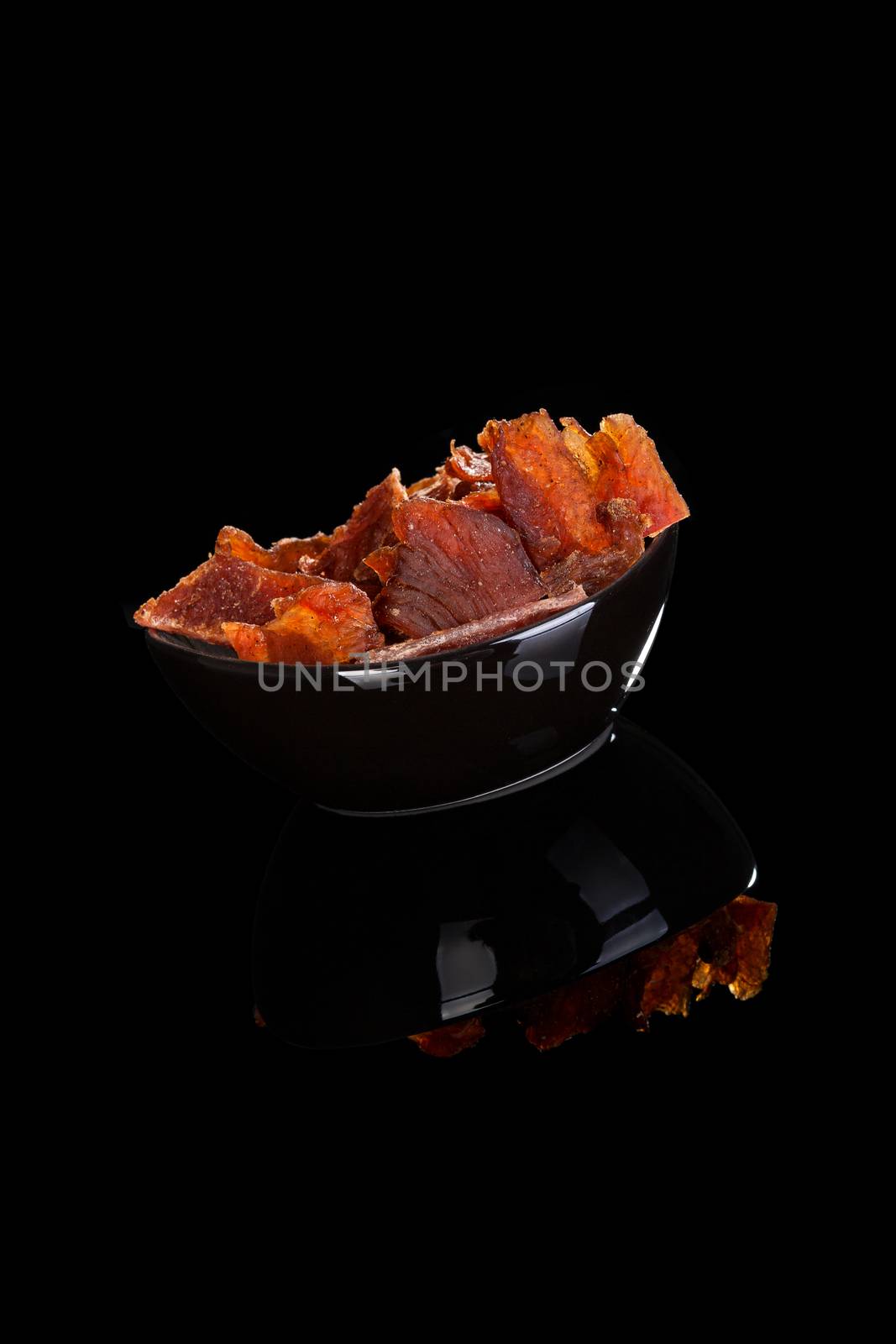 Beef jerky, dried meat in bowl isolated on black background. Culinary meat eating.