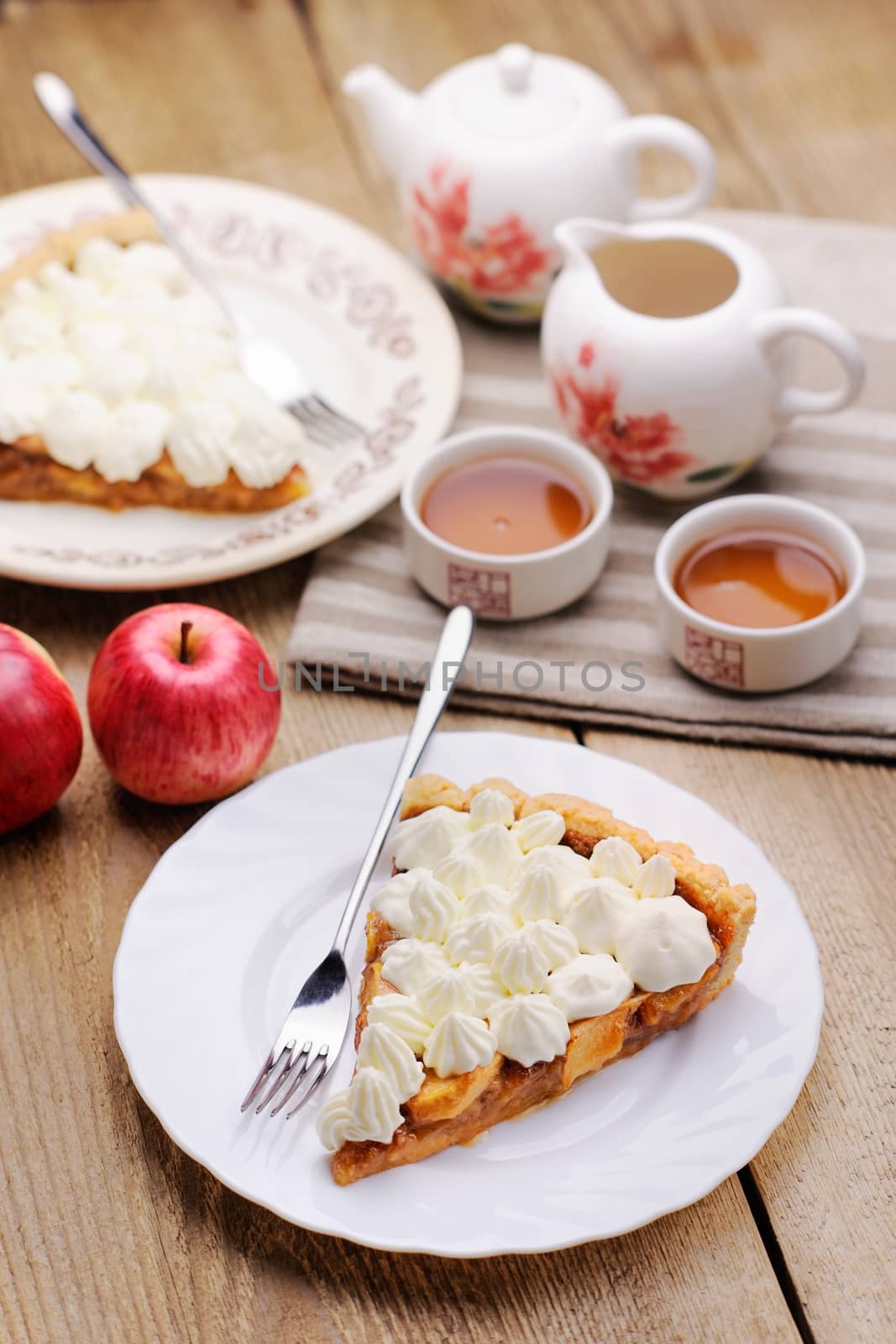 Apple tart with whipped cream, red apples and teaware on wood table