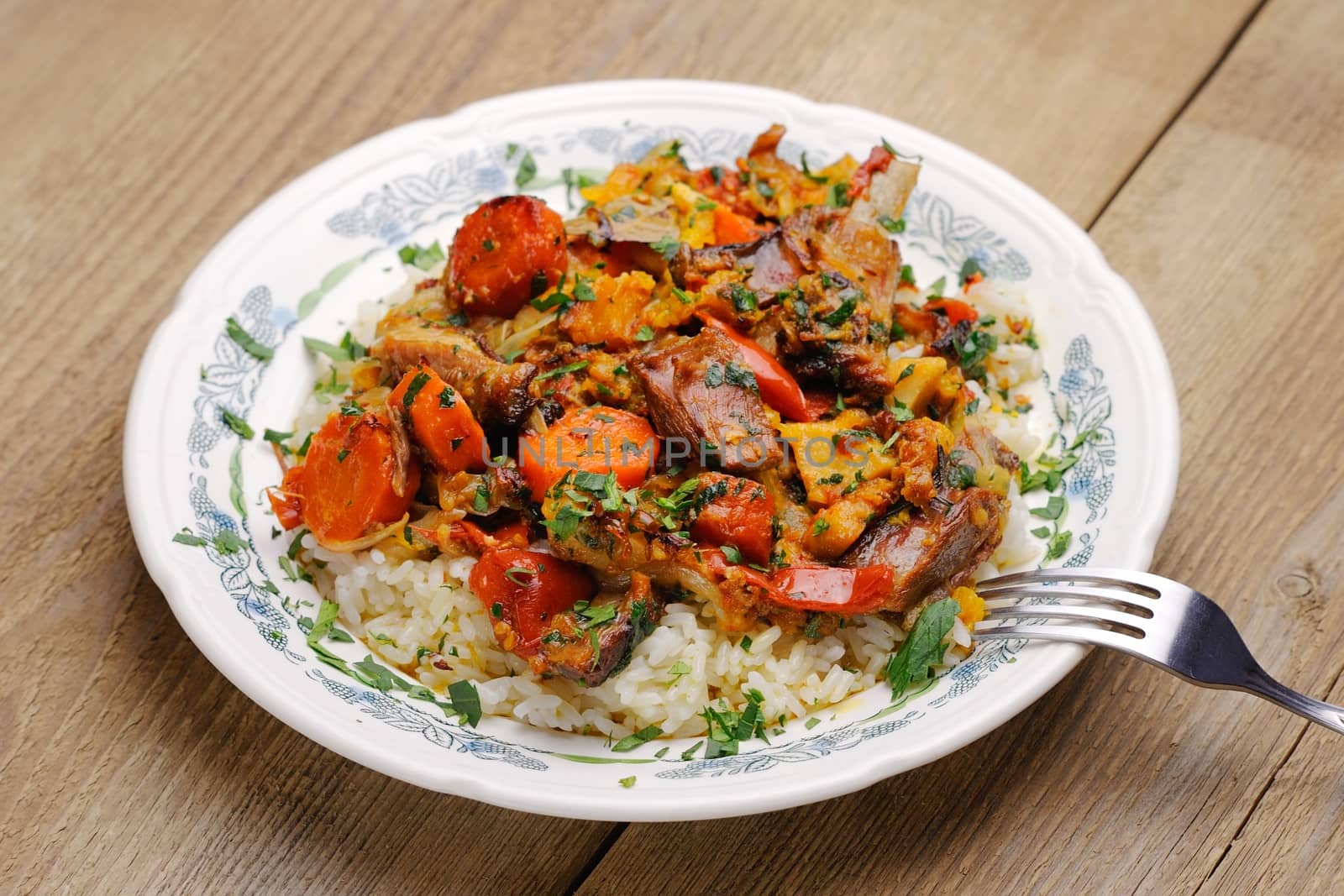 Lamb ragout with vegetables and rice in white plate on wooden background