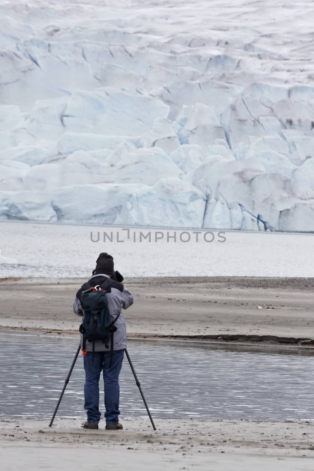 Active senior man wearing backpack and using a tripod photographs Mendenhall Glacier in Juneau, Alaska, in vertical image with copy space.