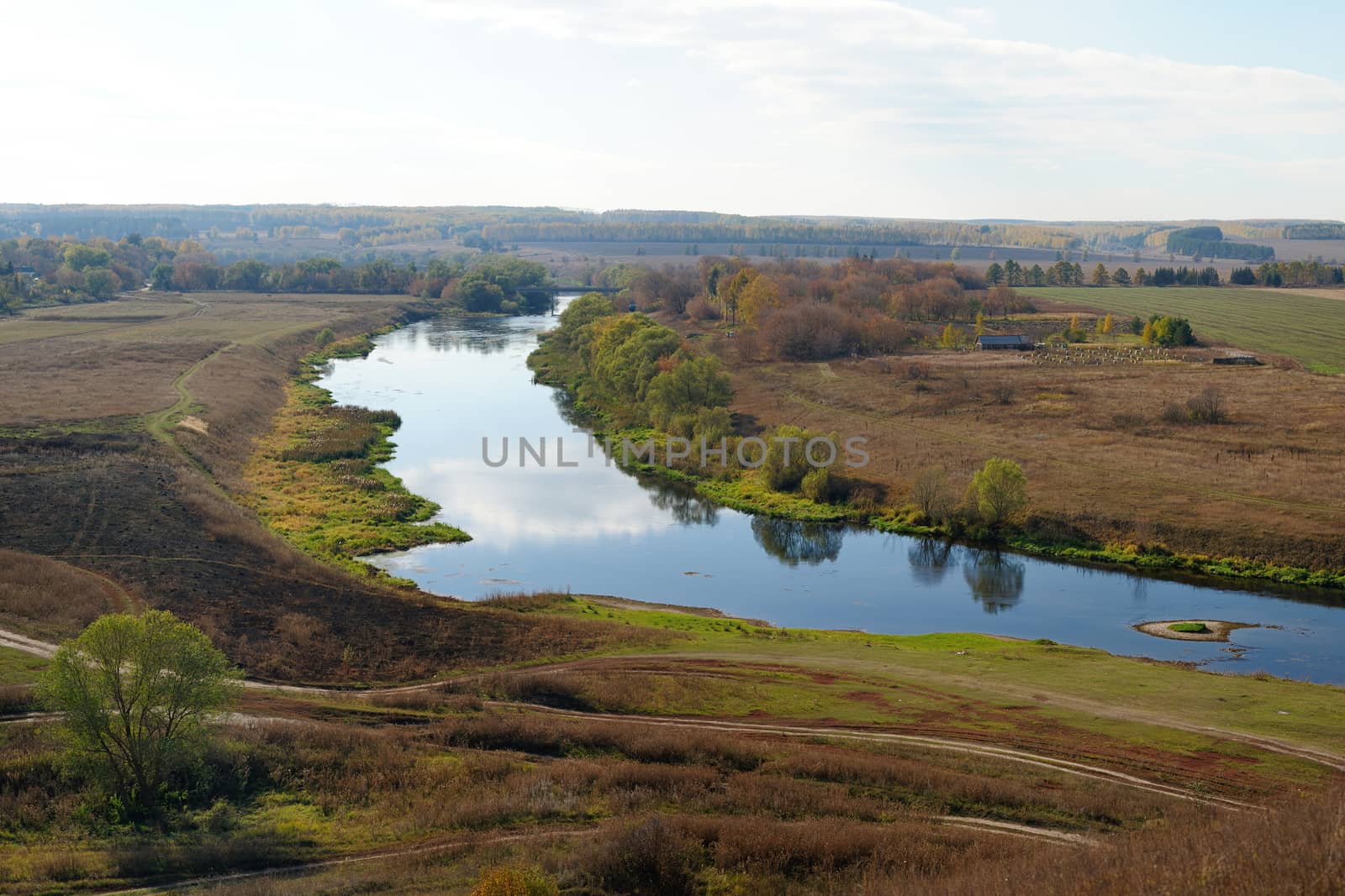 Autumn fields and narrow Zusha river with reflections of clouds