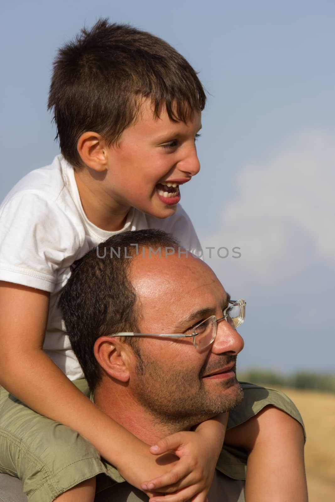 Cheerful child plays in the countryside on father's shoulders