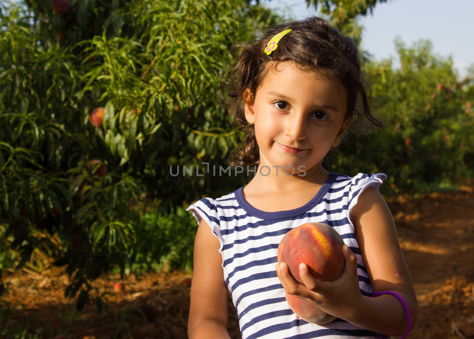 Cheerful little boy playing in the garden holding a peach