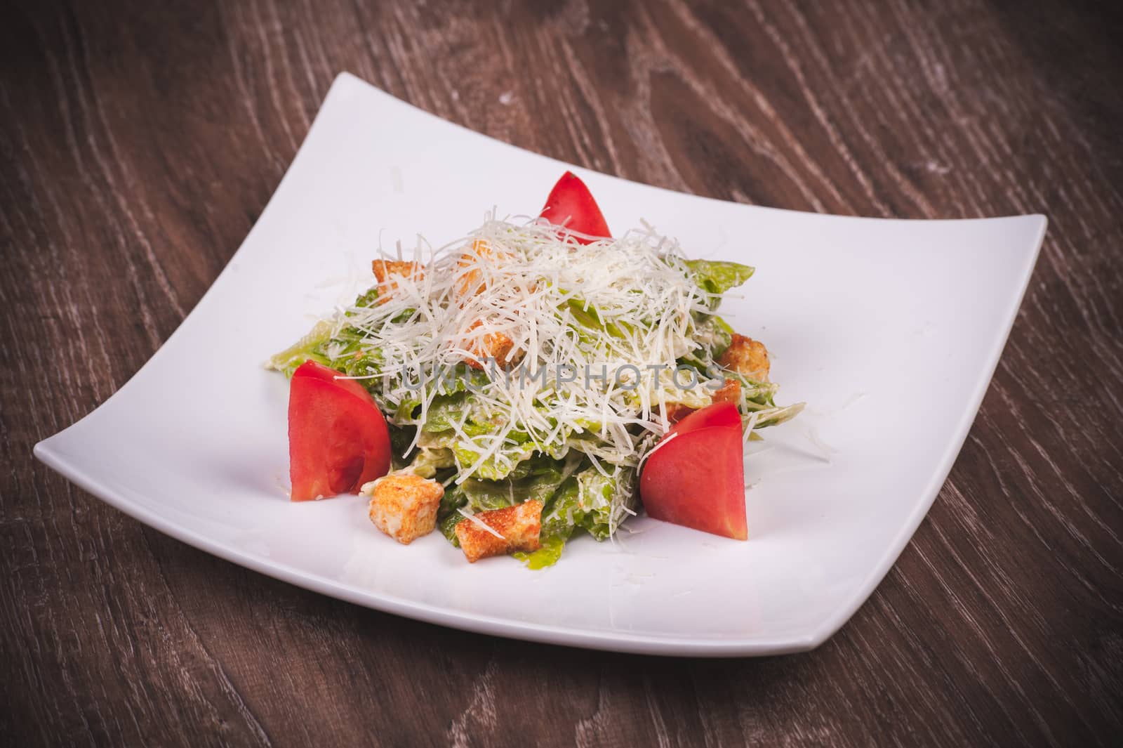 vegetarian cesar salad with tomato, croutons and cheese on white plate 