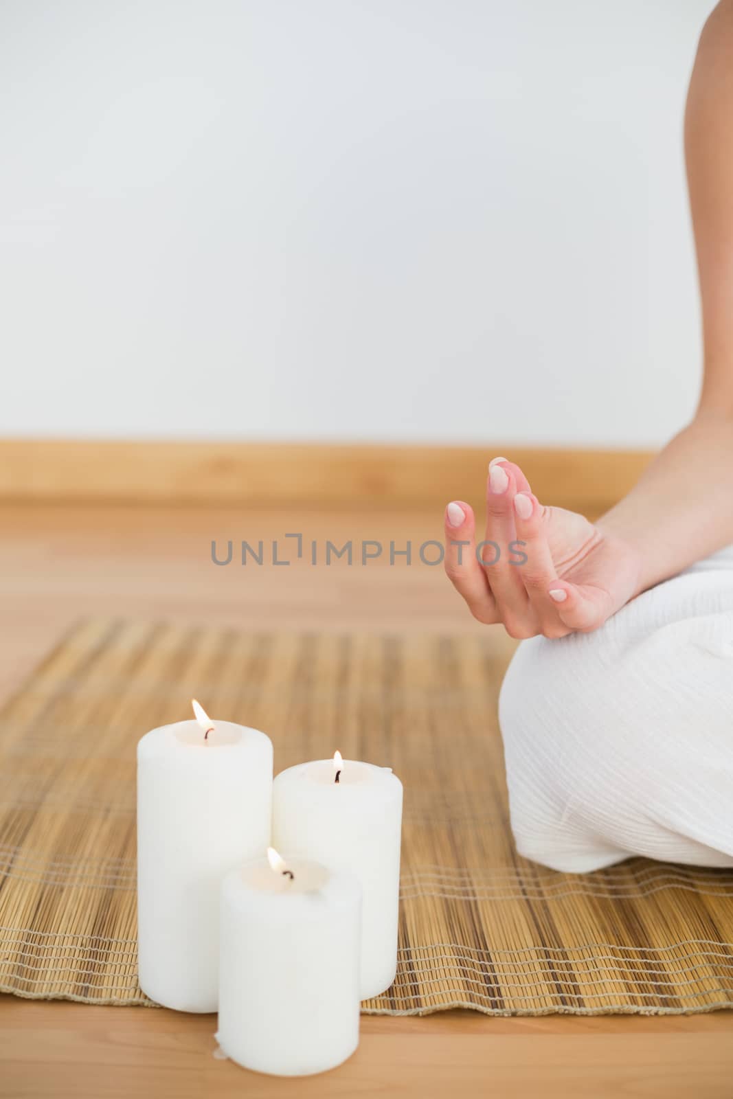 Woman sitting in lotus pose beside white candles in a white room
