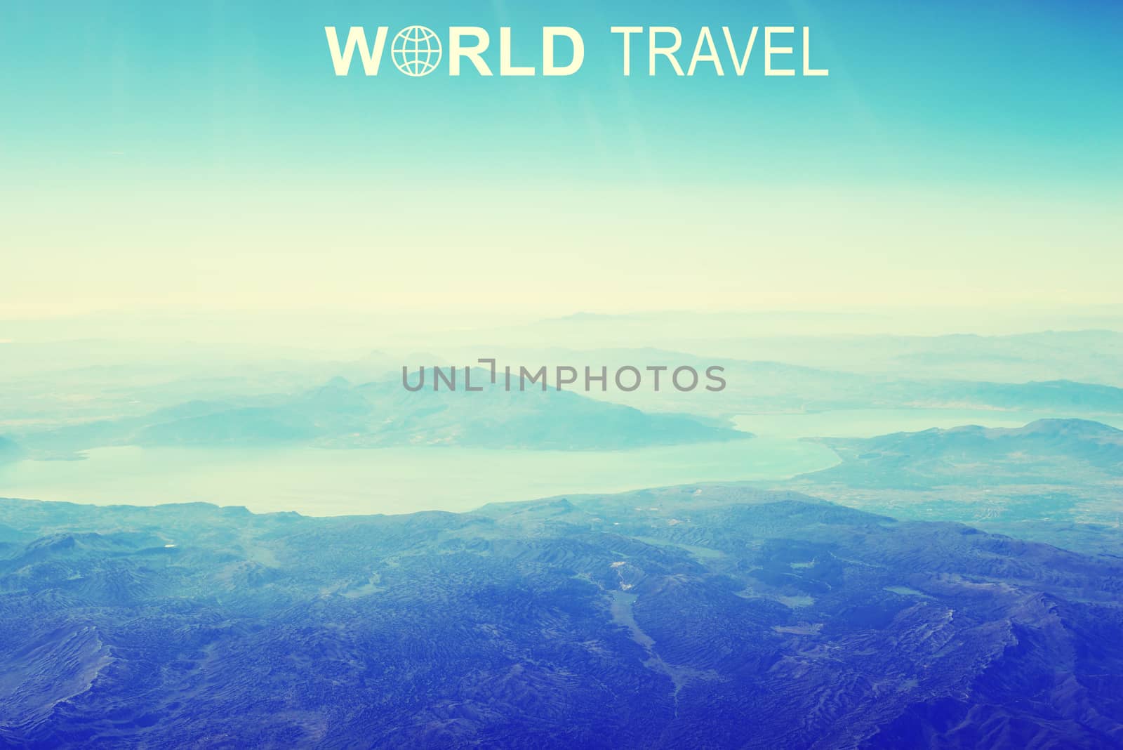 Aerial view of mountainous desert terrain, sky and clouds. Inscription World Travel and related symbol