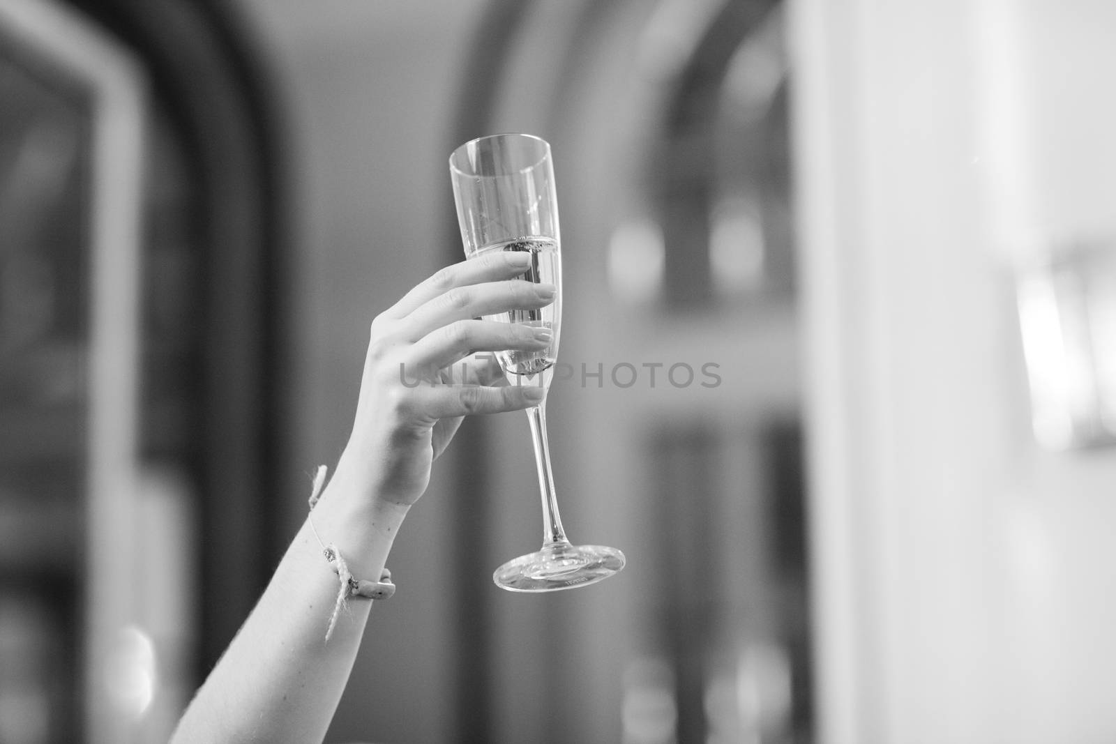 Black and white artistic digital rectangular horizontal photo of hand of young woman in wedding banquet marriage party holding sparkling white wine champagne flute glass in Madrid Spain. Shallow depth of with background out of focus. 