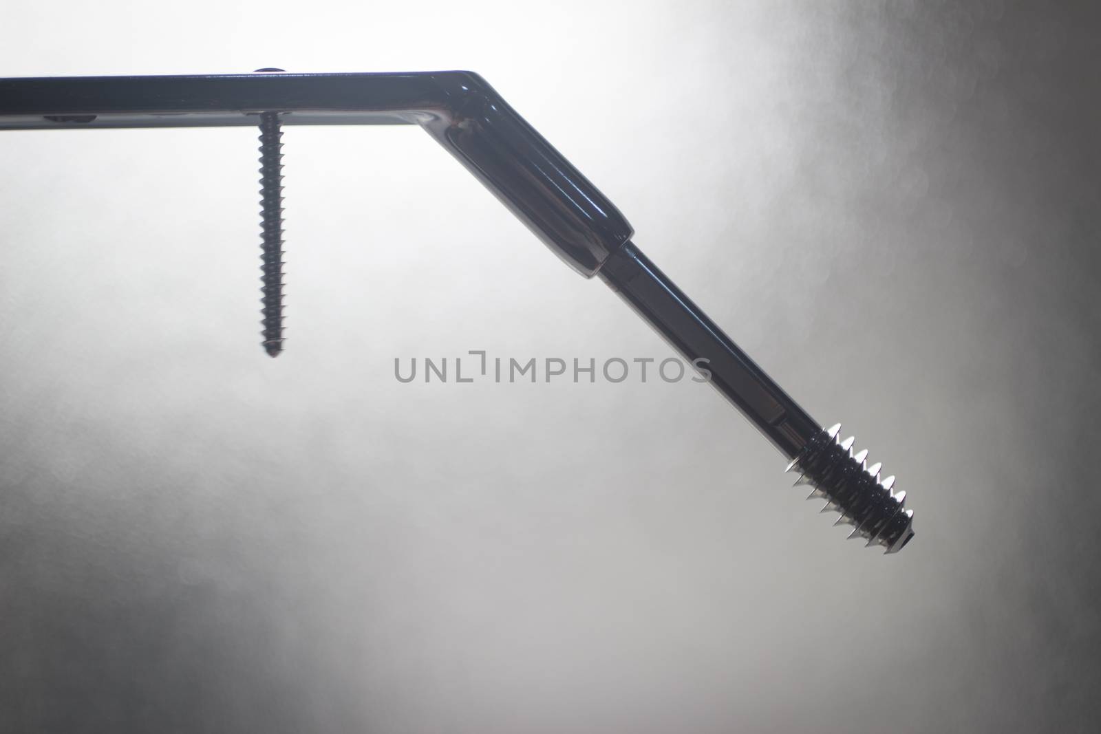 Traumatology orthopedic surgery plate and screw implant in semi silhouette against plain studio background. 