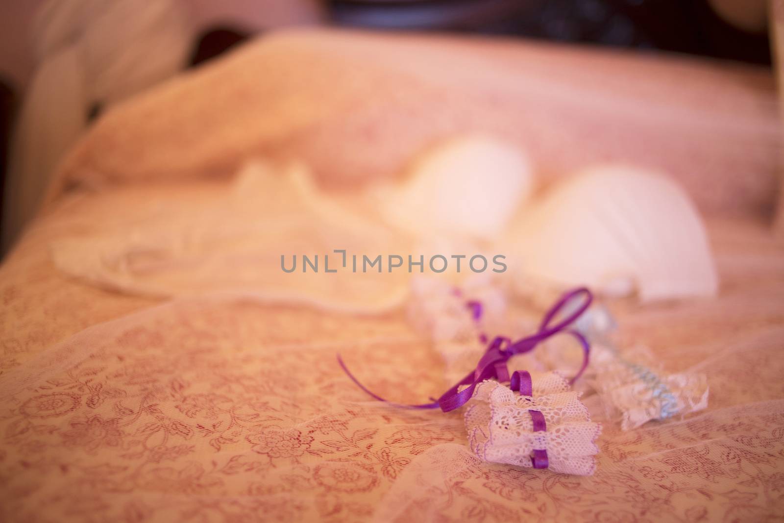 Color artistic digital rectangular horizontal photo of the bride's wedding bridal garter belt and bra underwear lingerie on bed. Shallow depth of focus with background defocused. 