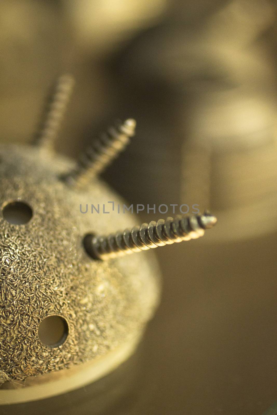 Closeup macro photograph of traumatology and orthopedic surgery metal hip ball joint implant with screw holes and screws against plain beige background defocused. 