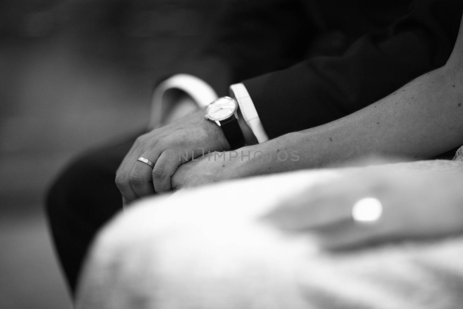 Black and white artistic digital rectangular horizontal photo of the bride wearing white wedding dress and bridegroom holding hands during church wedding marriage ceremony in Madrid Spain. Shallow depth of on foreground with background out of focus.