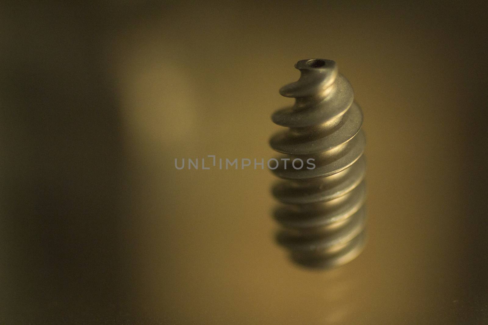 Traumatology orthopedic surgery implant titanium screw in semi silhouette against plain black studio background. Close-up macro horizontal photograph in brown warm tones. 