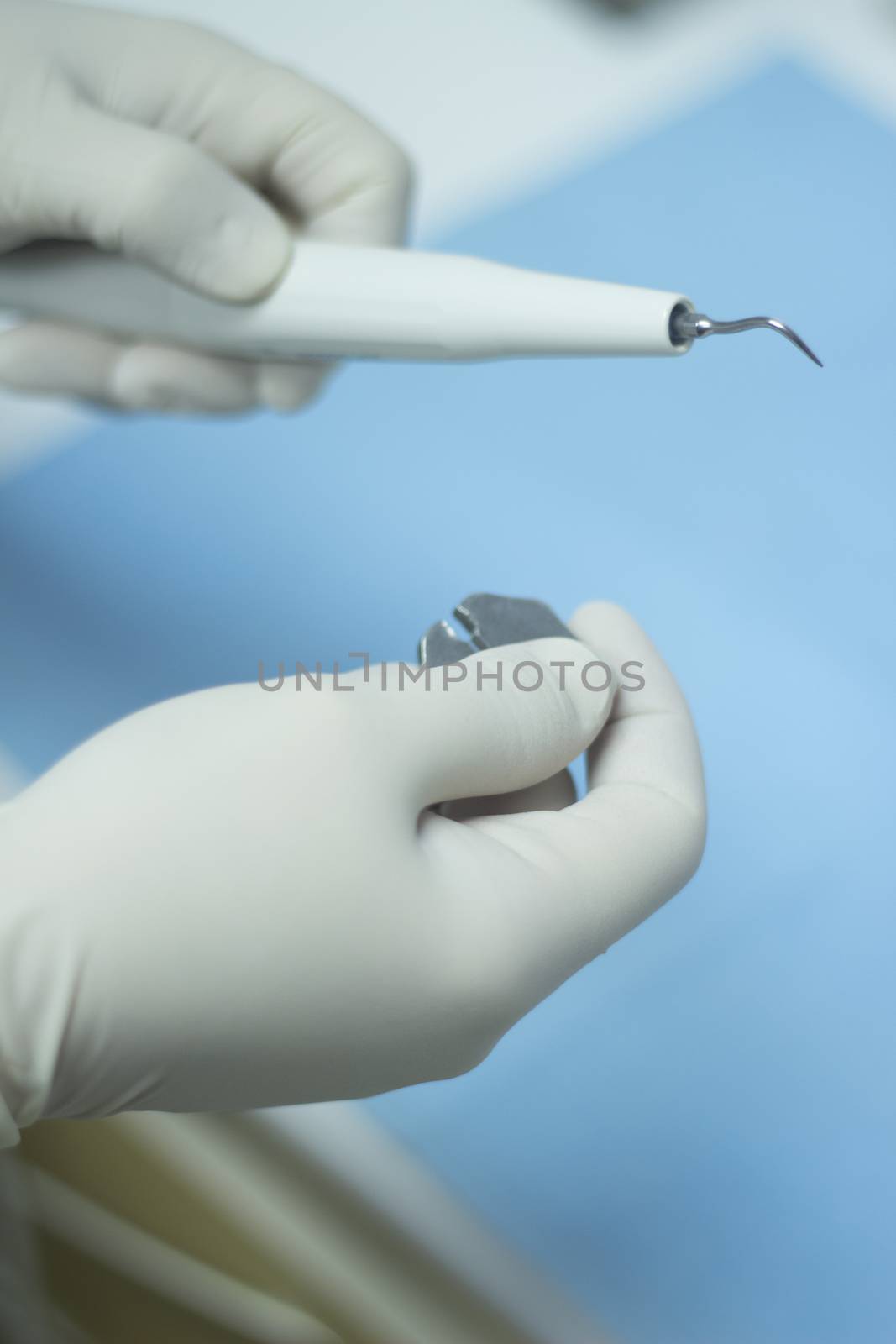 Hands of dental nurse in dental surgery clinic in white surgical sterile gloves attaching ultrasound teeth cleaning attachment prior to patient tooth clean treatment session by the dentist. Close-up photo with shallow depth of focus. 