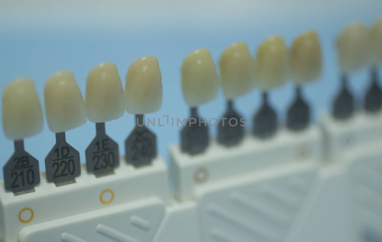 Dentist's tooth color guide used to choose the appropriate natural colors for a patient's tooth implants and crowns on plain blue background of the dental surgery clinic table. Close-up macro photo. 