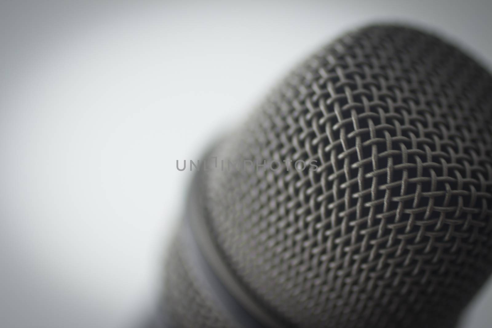 Professional studio voice recording microphone showing metallic body. Artistic color digital photo with shallow depth of focus and negative space and white blue grey background. 